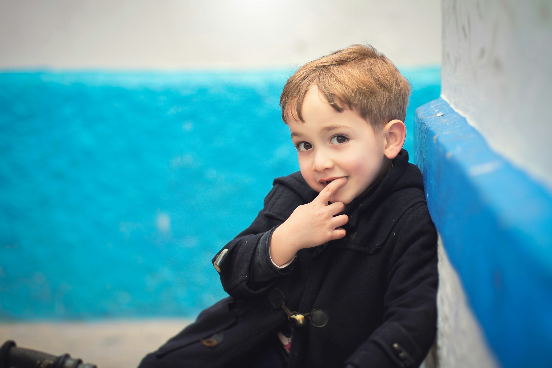 A child sitting beside a bright blue wall